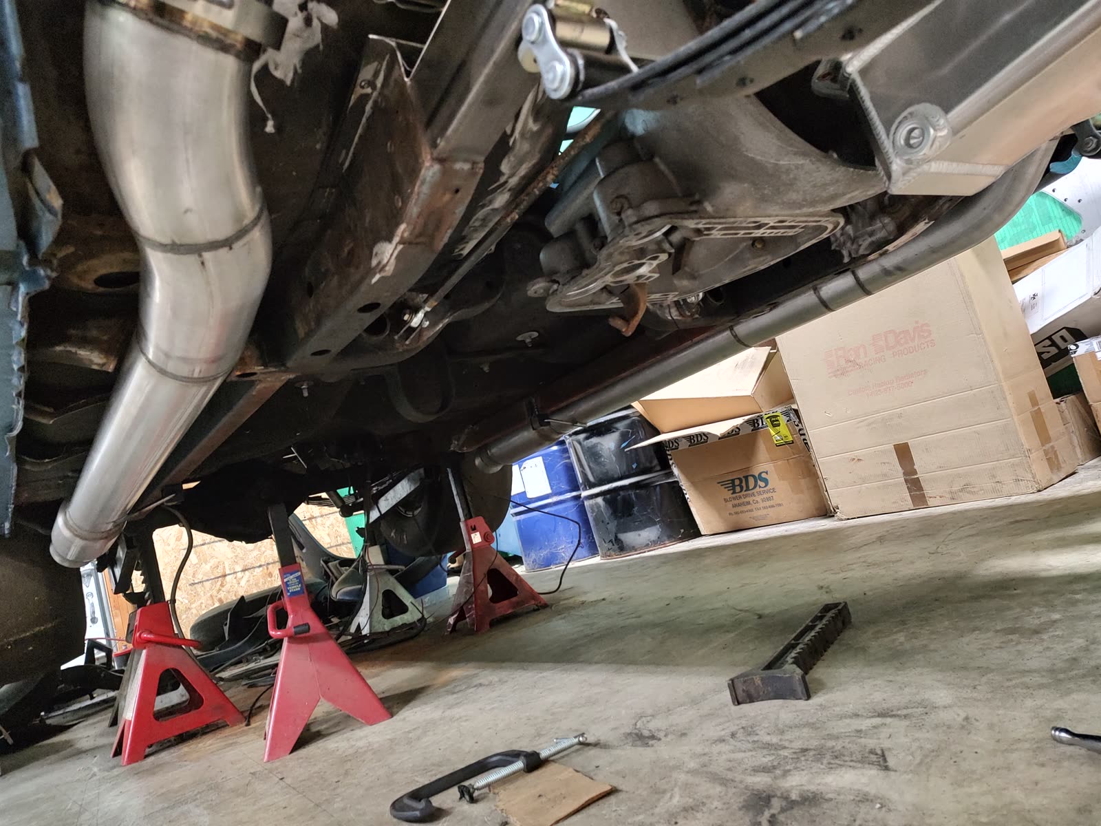 The underside of a vehicle up on jack stands, showing a newly fabricated stainless exhaust system running the length of the floor.