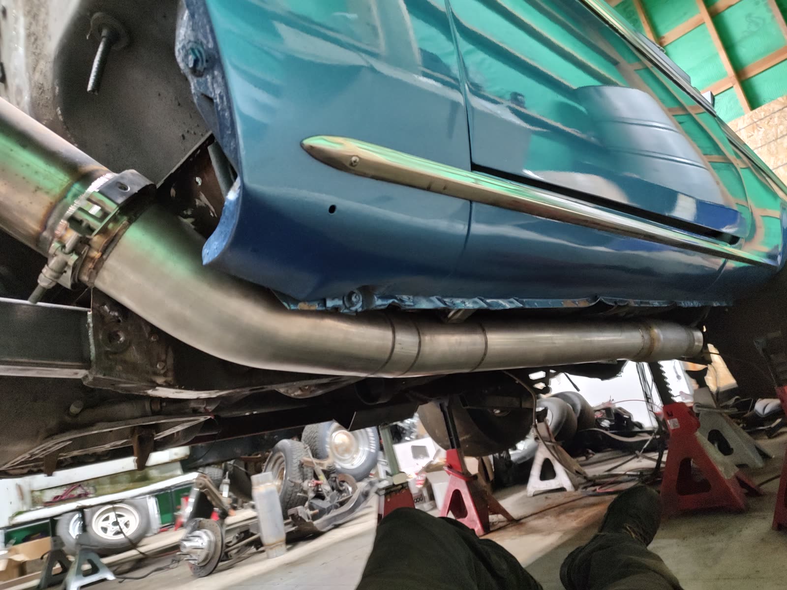 Looking up from beneath a teal classic car at a custom exhaust routed along the rocker panel.