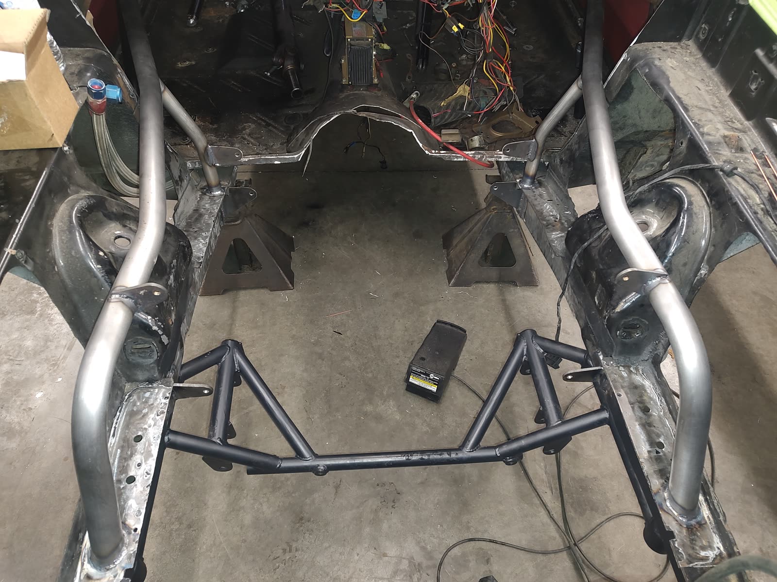 A bare frame-off chassis with custom tubular exhaust routed through it and the wiring harness still exposed.